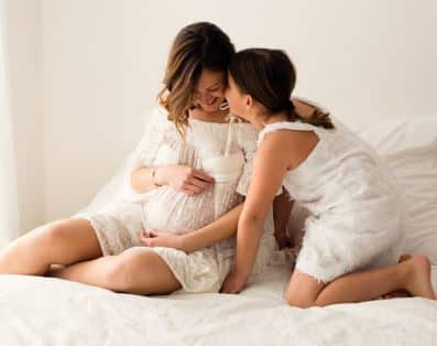 Donna incinta con figlia grande vestite con sottana bianca su letto matrimoniale con lenzuola bianche